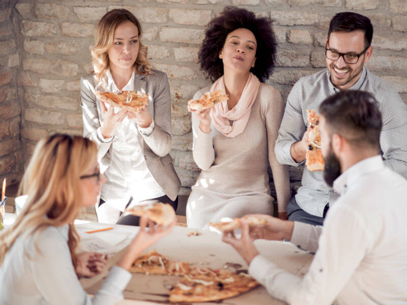 Fünf fröhliche Mitarbeiter essen zusammen eine Pizza